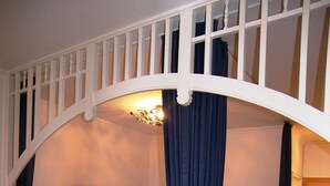 Ein Schlafzimmer mit einem Bett unter einer weißen Balkonkonstruktion, einem kleinen Nachttisch mit Lampe und einem Teppich auf dem Boden.