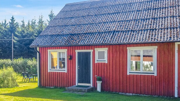 Une maison rouge avec un toit foncé, des fenêtres blanches et une porte noire.