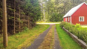 Un chemin de campagne menant à une grange rouge, entourée d’une forêt dense.