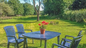 Un espace extérieur aménagé avec une table et quatre chaises, entouré d’une pelouse verdoyante et d’arbres.