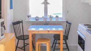 Une cuisine avec une table en bois, deux chaises noires, une fenêtre ornée de plantes en pot et un poêle blanc.