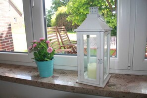 Ett fönster med en turkos kruka fylld med rosa blommor och en vit lykta med ett ljus inuti.
