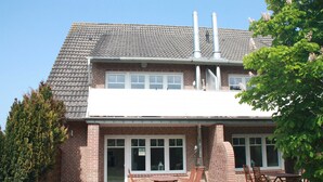 Ein zweistöckiges Backsteinhhaus mit einem Ziegeldach, einer Terrasse mit Holzmöbeln und einem Schornstein.