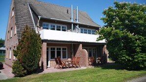 Ein zweistöckiges Haus mit Ziegelaußenwand, einer überdachten Terrasse mit Gartenmöbeln und einem großen Baum im Vorgarten.