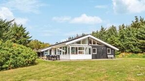 Une maison moderne dotée d’un grand patio, d’un espace salon extérieur couvert et offrant une vue sur une zone boisée.
