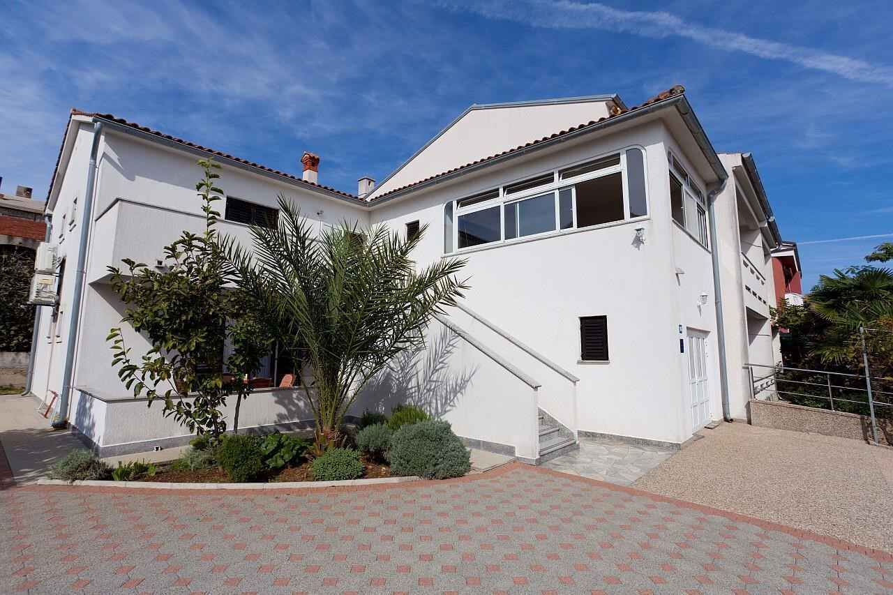 Una casa bianca a due piani con tetto in tegole, una piccola scala e un vialetto lastricato.