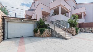 A multi-story residential building with a stone facade, a garage, and a staircase leading to the upper floors. - Holiday apartment with air conditioning and sea view (Klimno)