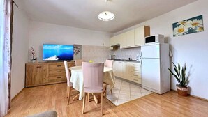 En kompakt opholdsstue med spiseplads, køkken og et fjernsyn, der viser et smukt landskab.