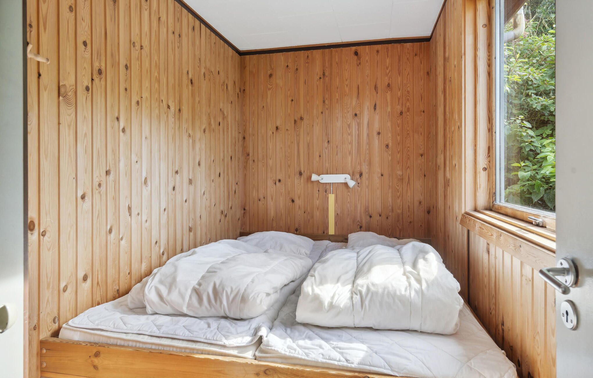 A single bed with white bedding in a room with wooden walls and a window.