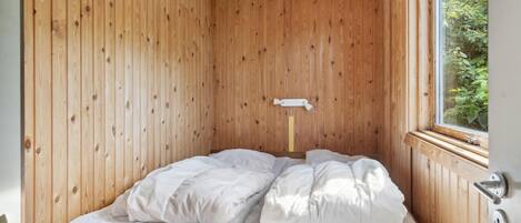 A single bed with white bedding in a room with wooden walls and a window.