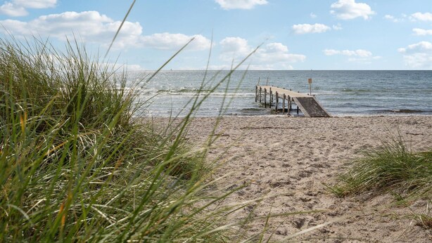 A beach with a wooden pier extending into the water, surrounded by sand and grass. - Nice home in Sydals with WiFi (Sydals)