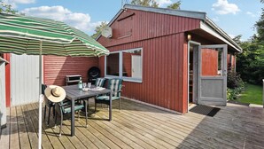 A wooden deck with a table and chairs, a striped umbrella, and a red building with a door and windows. - Nice home in Sydals with WiFi (Sydals)