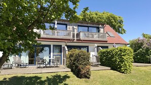 A two-story building with a balcony, outdoor seating area, and a well-maintained lawn. - Vacation apartment 07 south facing with sea view - P: Zollhaus Klein Zicker - exclusive (Thiessow)