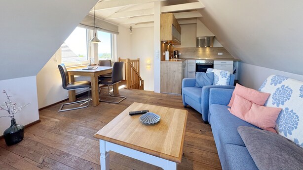 A cozy loft-style living space with a dining area, kitchenette, and a large window providing natural light. - Vacation apartment 07 south facing with sea view - P: Zollhaus Klein Zicker - exclusive (Thiessow)