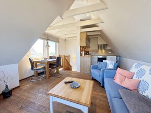 Un espace de vie chaleureux de style loft, comprenant un coin repas, une kitchenette et une grande fenêtre laissant entrer la lumière naturelle.