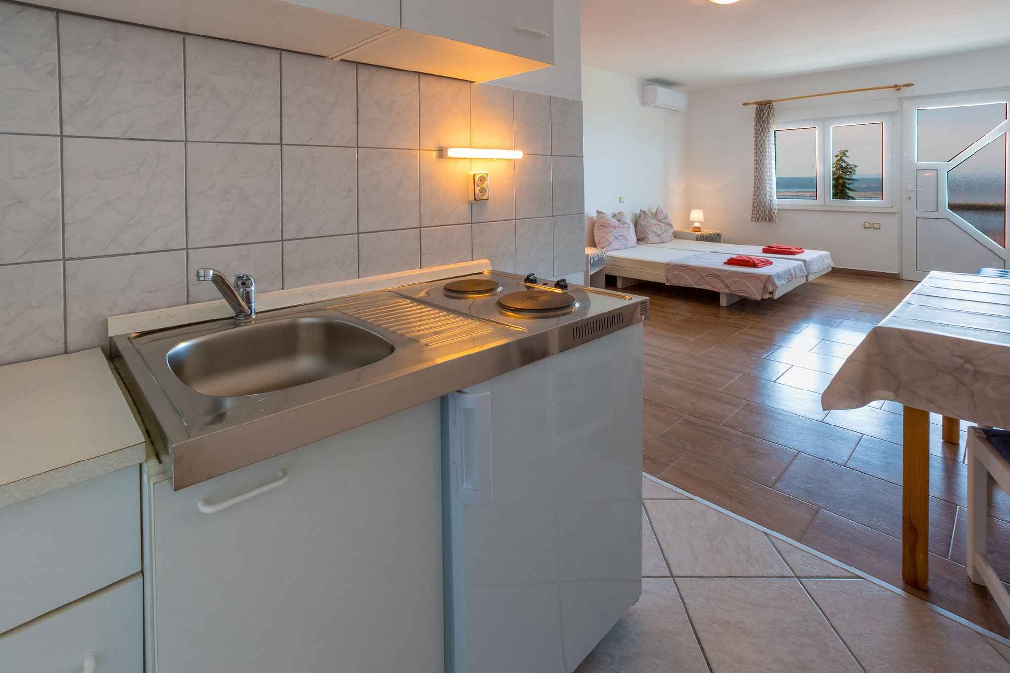 A compact kitchen with a built-in sink and stove, a dining area with a table, and a bedroom with a bed and window.