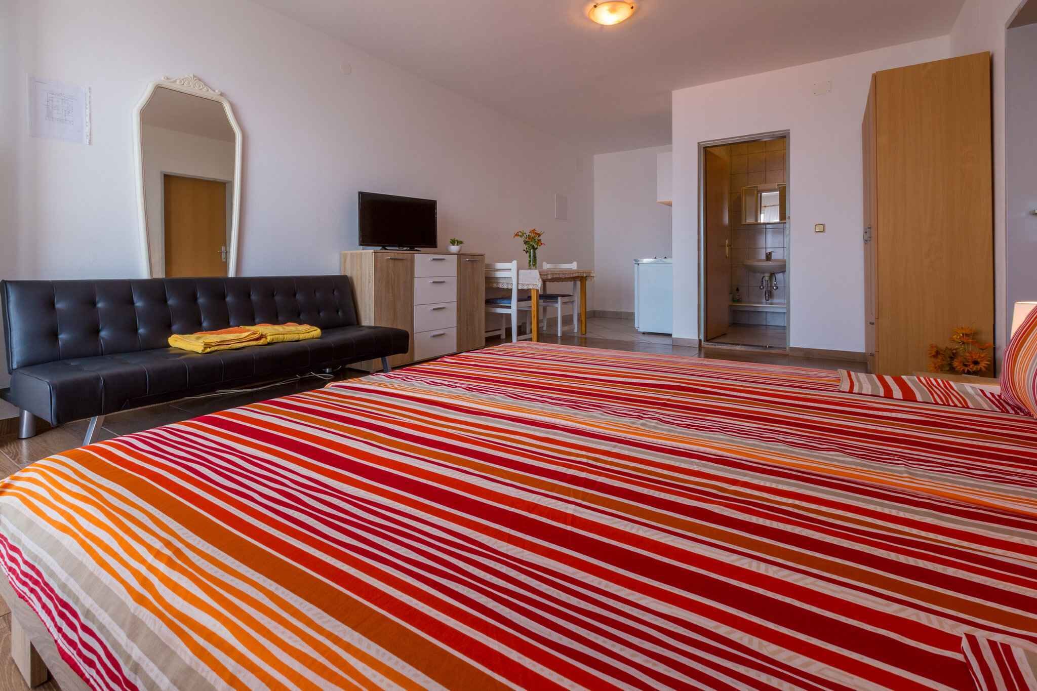 Une chambre à coucher avec un grand lit, un canapé, une télévision, un bureau et une salle de bain visible à travers une porte ouverte.