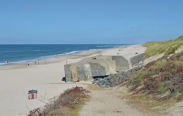 A beach with a concrete structure featuring graffiti, a sandy path, and the ocean in the background.