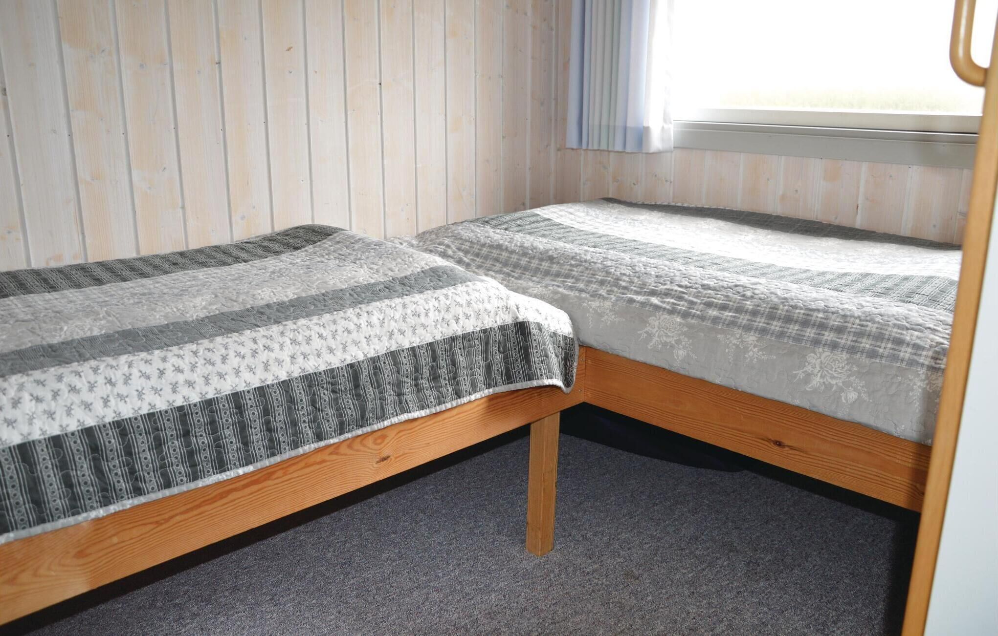 A room with two wooden bunk beds, a window with blinds, and a light-colored wall.
