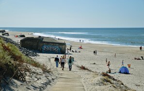 A beach with a wooden walkway leading to the water, a large graffiti-covered structure, and people enjoying the beach.