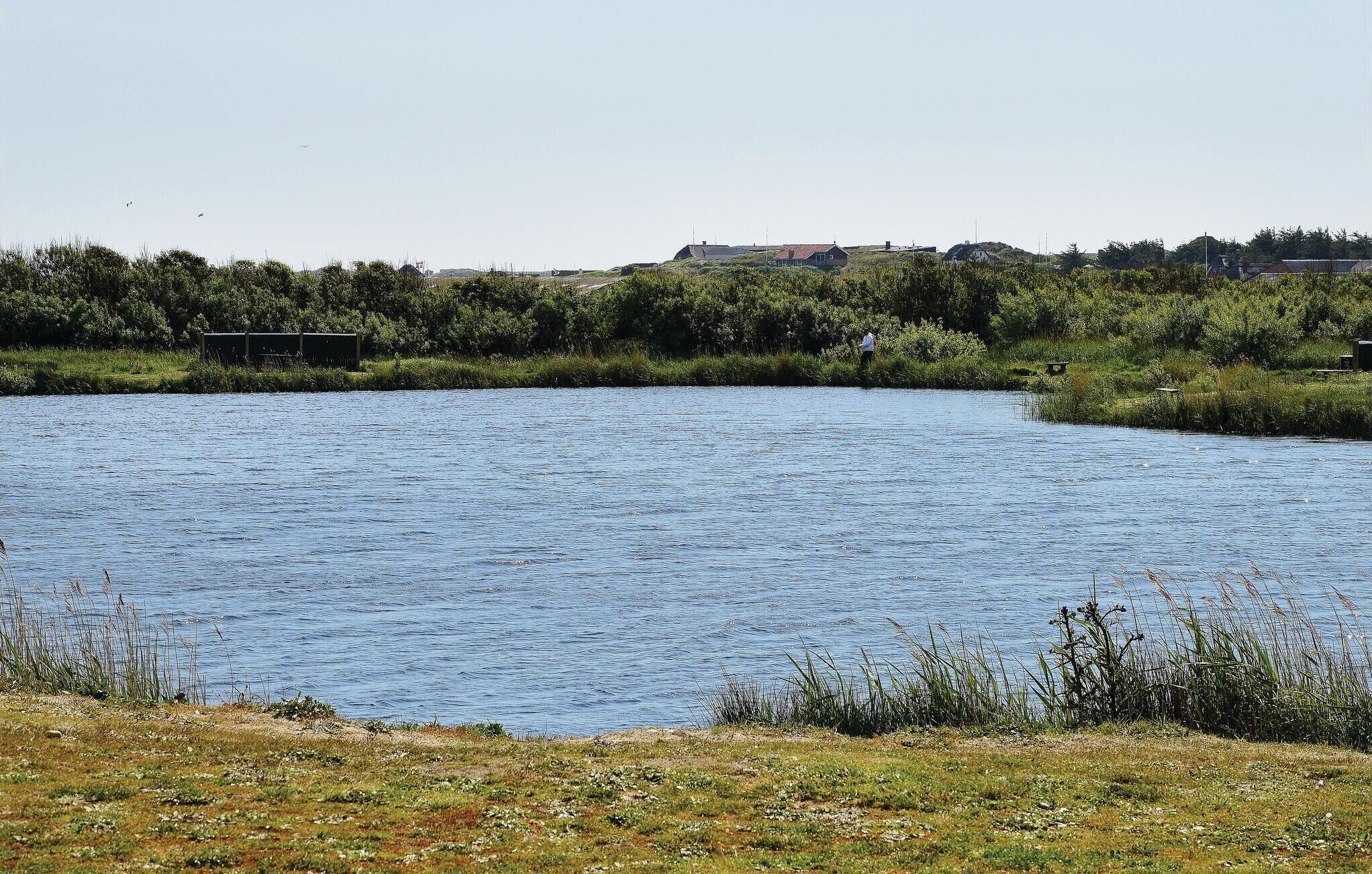 Une rivière paisible, bordée d’une rive verdoyante, avec quelques bâtiments visibles au loin.