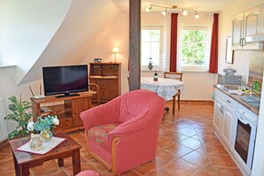 Una sala de estar acogedora con televisor, un sillón rojo, una mesa de madera y una zona de cocina con estufa y armarios.
