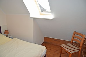 A bedroom with a skylight, a wooden chair, and a bed with a white duvet. - 04 Vacation apartment with lake view - Karolas Landhus under the thatched roof (Mönchgut)