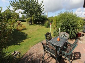 Een terras met een tafel en stoelen, omringd door begroeiing en een boom.