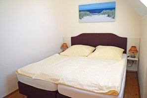 A single bed with a headboard, two bedside lamps, and a painting of a beach scene on the wall.