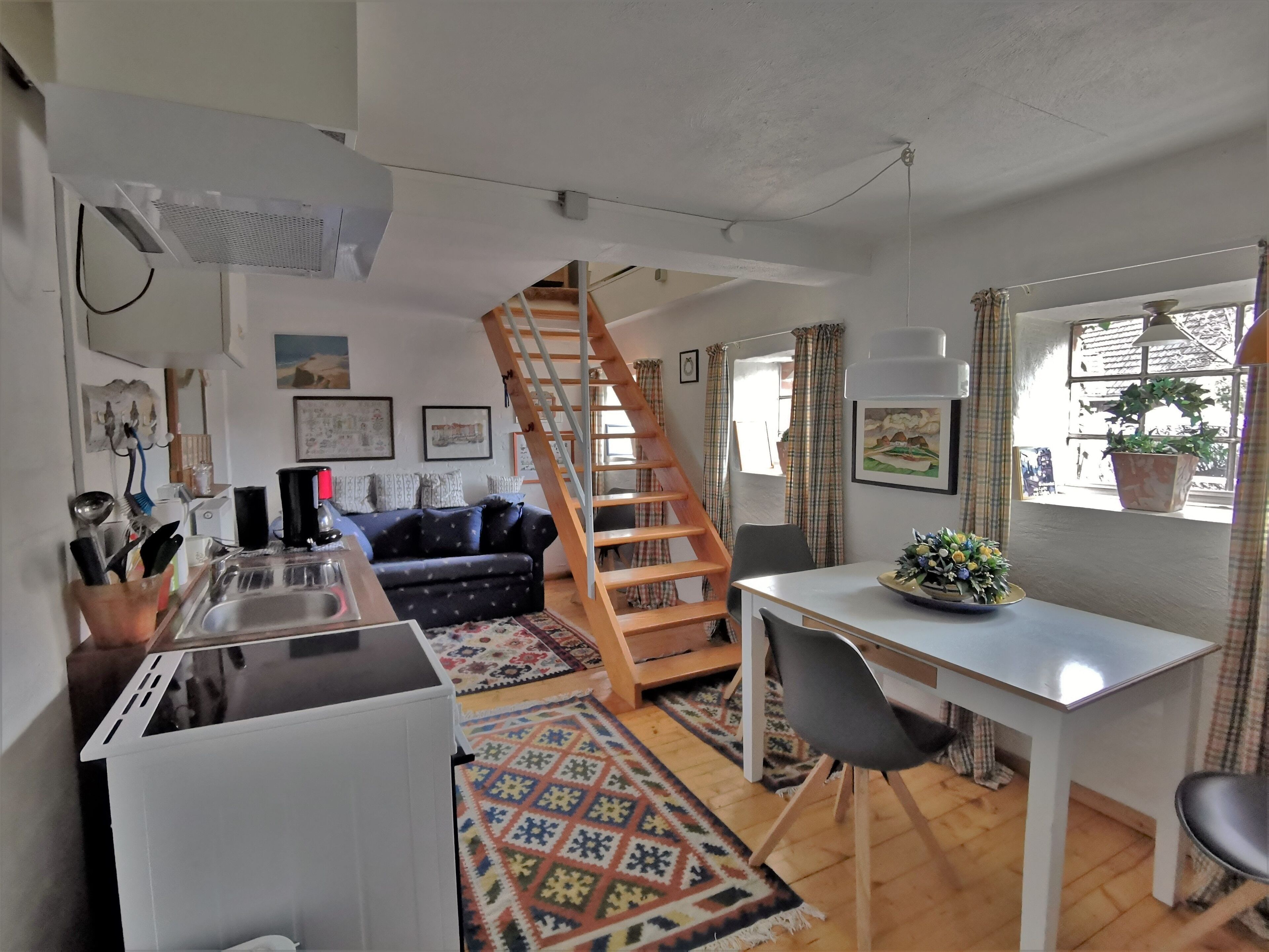 A compact living space with a kitchenette, a dining area, a staircase, and a window with a plant.