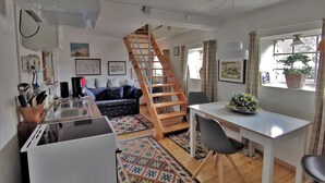 Ett kompakt bostadsutrymme med ett litet kök, en matplats, en trappa och ett fönster med en växt.