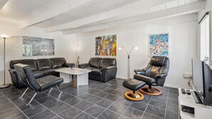 A modern living room with a black leather sofa, a coffee table, and a leather armchair. There are abstract paintings on the walls and a flat-screen TV on the right. - Awesome apartment in Rømø with WiFi (Rømø)