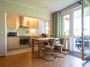 A modern kitchen with wooden cabinets, a built-in microwave, and a dining area with a wooden table and two chairs. - Dune garden Whg. Wa45-41 - Wa45-41 (Kühlungsborn)