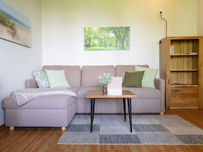 A living room with a sofa, a small table with a vase, a bookshelf, and a painting on the wall. - Dune garden Whg. Wa45-41 - Wa45-41 (Kühlungsborn)