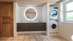 A bathroom with a wooden door, a round mirror, a dark wooden vanity, a washing machine, and a window. - Nice home in Jerup with kitchen (Jerup)