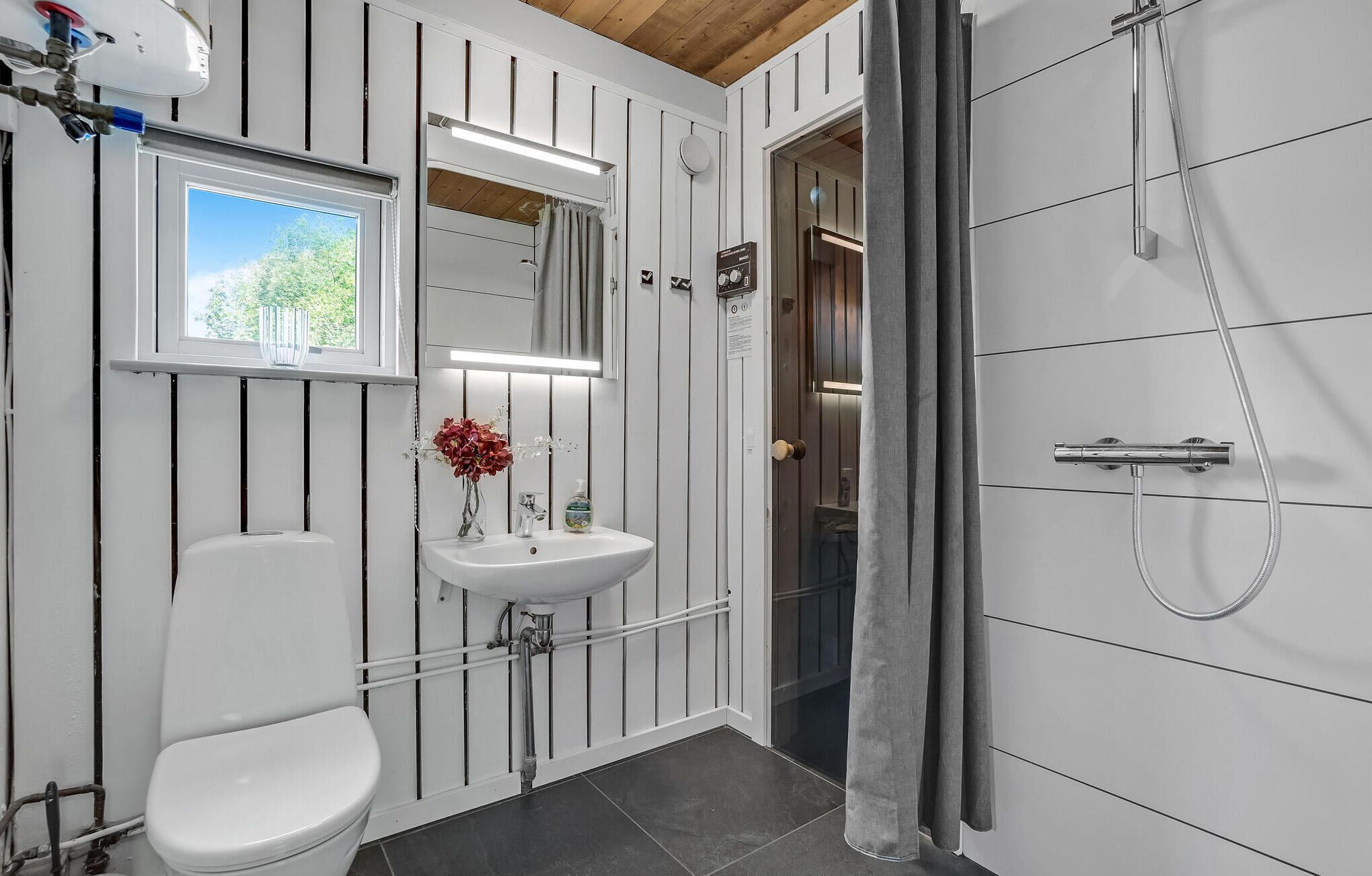 Een badkamer met toilet, wastafel, douche en een raam.