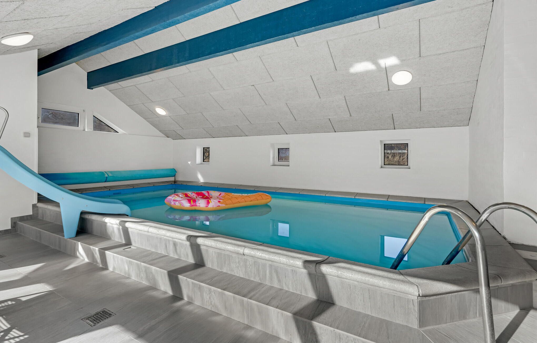 Ein Hallenbad mit einer blauen Rutsche, einem Schwimmreifen und einer Treppe zum Pool.