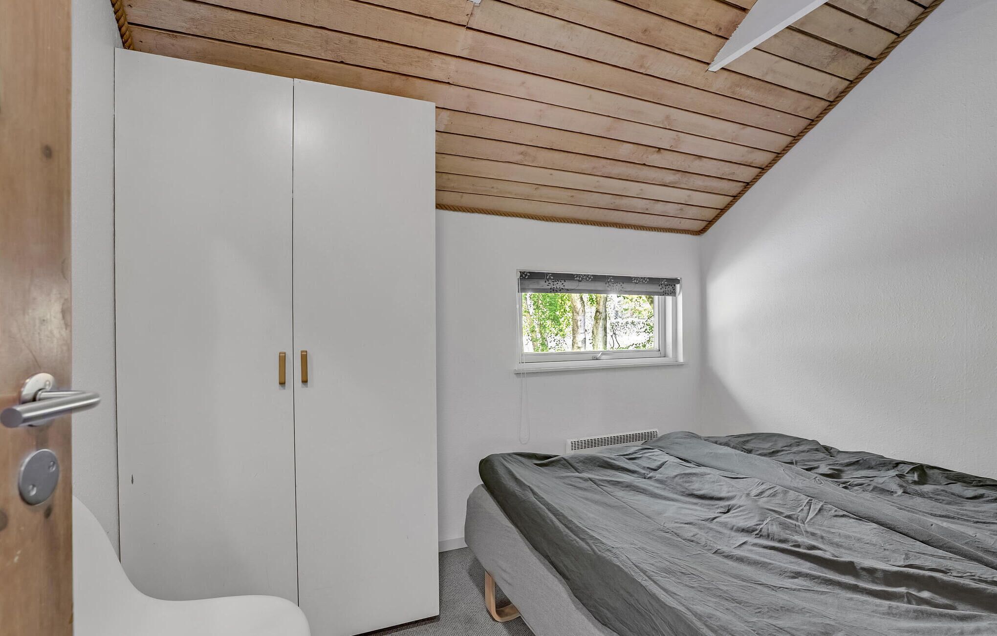 Een slaapkamer met een bed, een kledingkast, een raam en een plafond met houten balken.