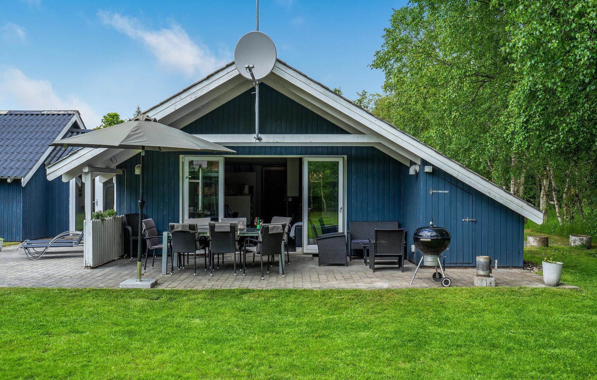 Et hus med terrasse, udendørs møbler og grill.