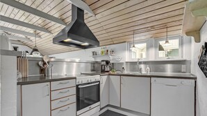 A modern kitchen with white cabinets, stainless steel appliances, and a wooden ceiling.