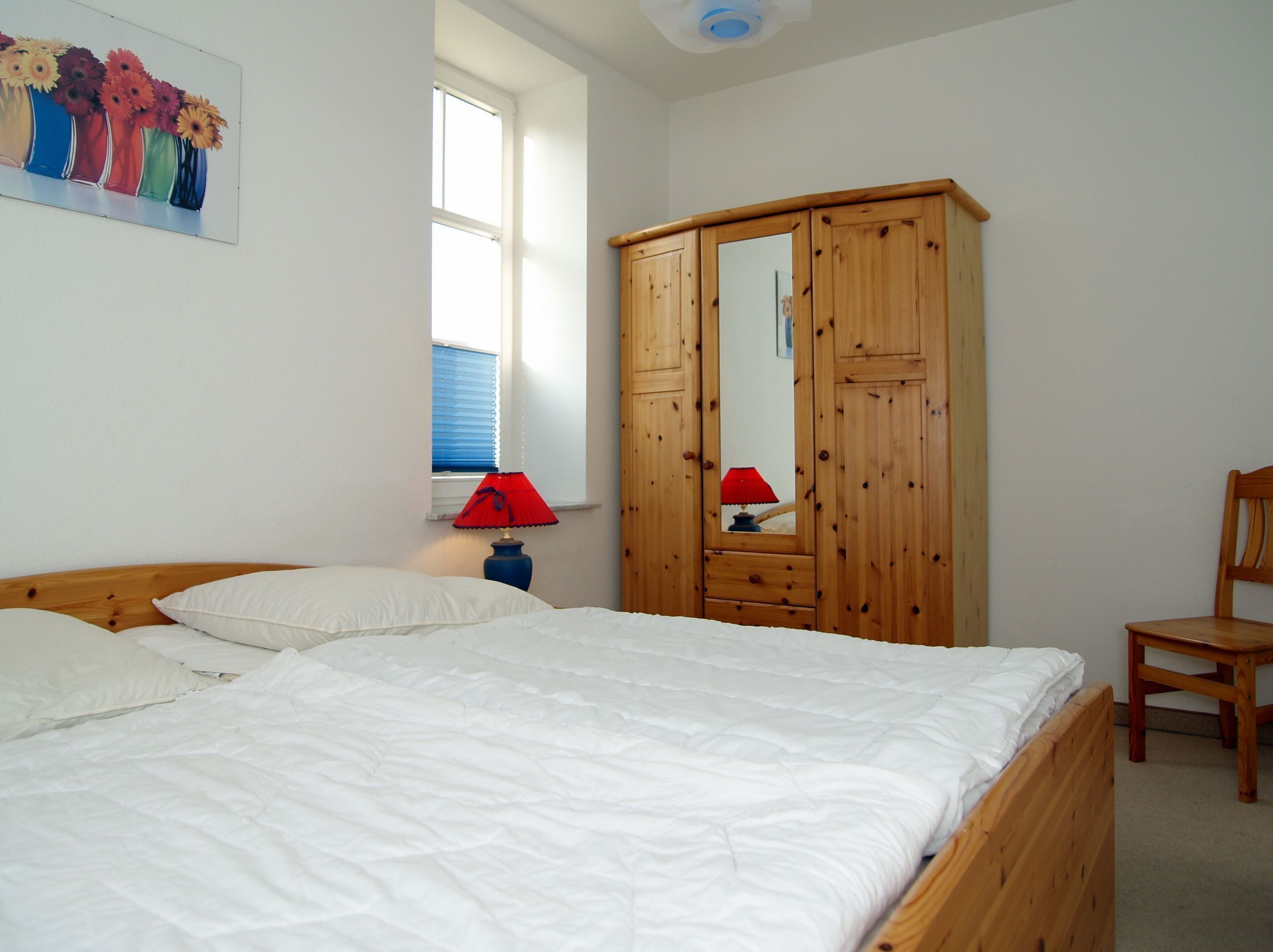 Un dormitorio con cama, un armario de madera, una silla y una ventana con persianas.