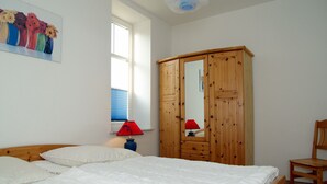 Um quarto com cama, guarda-roupa de madeira, uma cadeira e uma janela com persianas.
