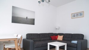 Uma sala de estar moderna com um sofá cinzento, uma mesa de centro branca, uma mesa de jantar de madeira com cadeiras e um quadro na parede.
