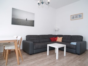 Un salon moderne avec un canapé gris, une table basse blanche, une table à manger en bois avec des chaises, et un tableau encadré accroché au mur.