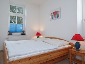 Une chambre à coucher avec un lit en bois, une fenêtre avec des stores, une table de chevet avec une lampe et un tableau accroché au mur.
