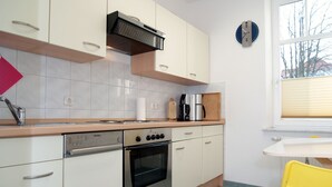 Uma cozinha moderna com armários brancos, forno de aço inoxidável, cafeteira e uma cadeira amarela.