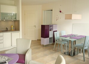 Eine moderne Küche mit weißen Schränken, einem Esstisch mit Glasplatte und einem violetten Schrank.
