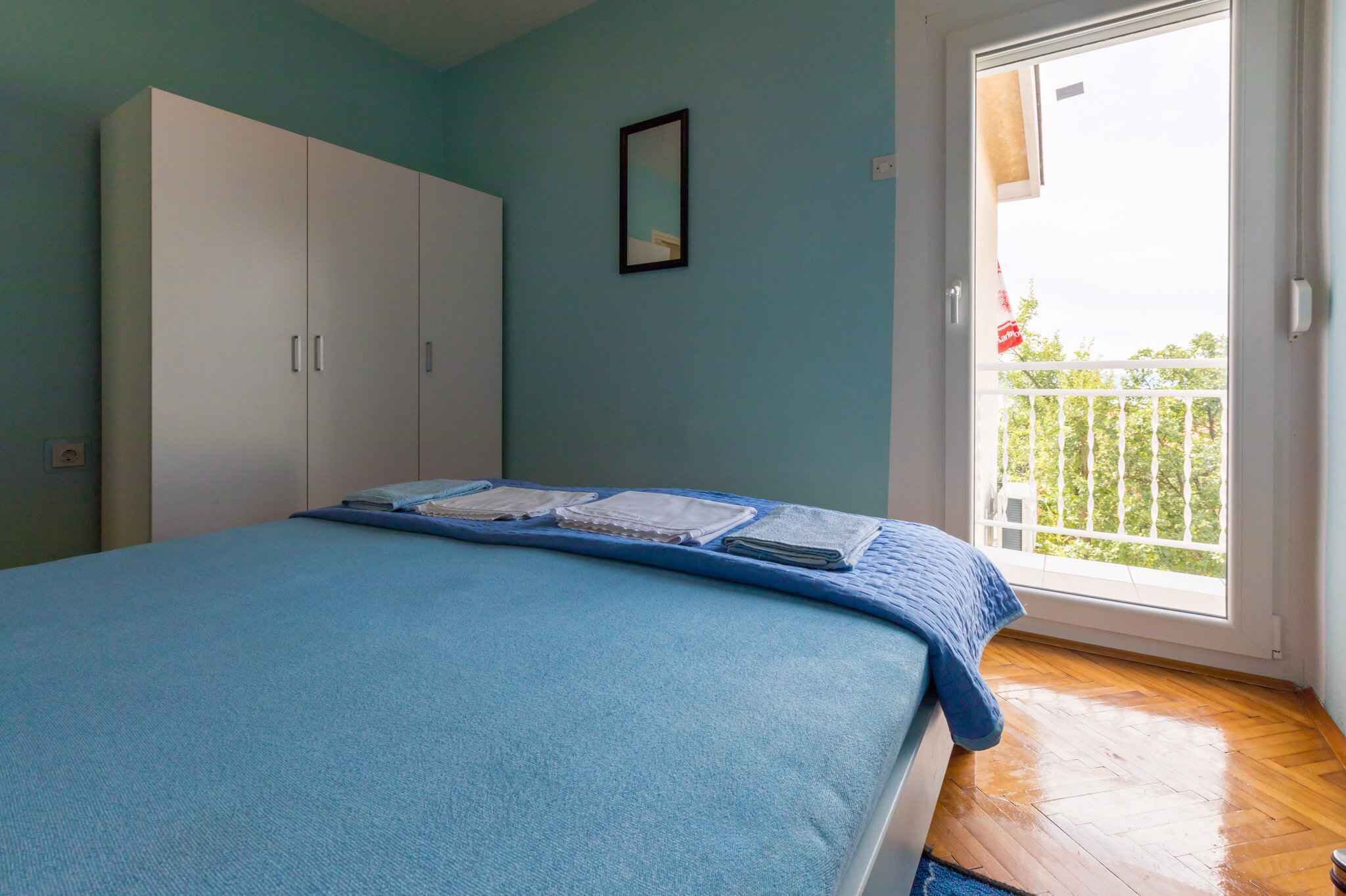 A bedroom with a bed, a wardrobe, a balcony with a view, and a framed picture on the wall.