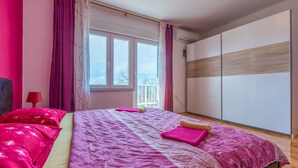 Een slaapkamer met een groot bed, roze beddengoed, een raam en een garderobe.