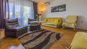 Een woonkamer met een bank, een fauteuil, een tafel met een bloevas en een schilderij aan de muur.